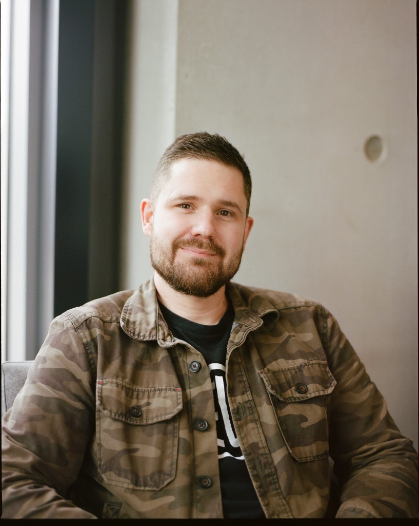 Portrait of Sam Reid, Co-Founder & CEO of EngineLab, seated in front of a concrete wall.