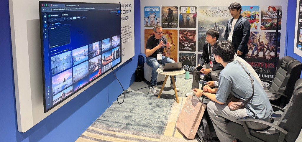 A presenter with a laptop shows the EngineLab AI gallery on a large wall screen to a small seated audience in the AWS Loft at IBC 2026.
